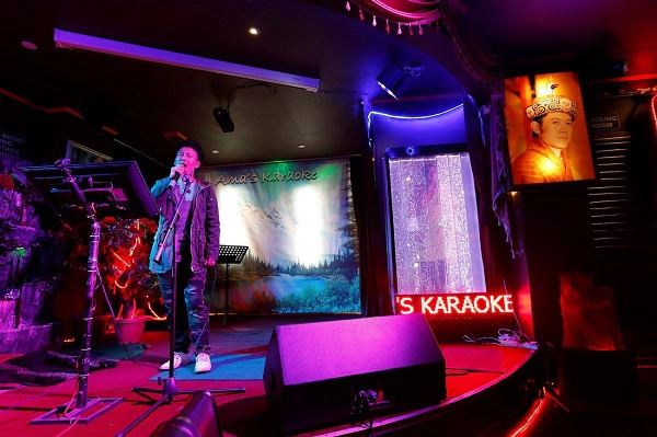 Một người đàn ông đang hát karaoke ở quán bar, cạnh bên phải là bức chân dung của Quốc vương Bhutan Jigme Khesar Namgyel Wangchuck (sinh năm 1980). Một người đàn ông đang hát karaoke ở quán bar, cạnh bên phải là bức chân dung của Quốc vương Bhutan Jigme Khesar Namgyel Wangchuck (sinh năm 1980).