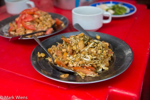 Các lá trà muối chua chua, đắng được trộn với bắp cải thái sợi, cà chua, đậu rán giòn, các loại hạt, một chút dầu tỏi, ớt và tỏi tươi thái lát. Món này có thể dùng ăn vặt, khai vị hoặc ăn kèm với cơm. Ảnh: Mark Wiens. Các lá trà muối chua chua, đắng được trộn với bắp cải thái sợi, cà chua, đậu rán giòn, các loại hạt, một chút dầu tỏi, ớt và tỏi tươi thái lát. Món này có thể dùng ăn vặt, khai vị hoặc ăn kèm với cơm. Ảnh: Mark Wiens.
