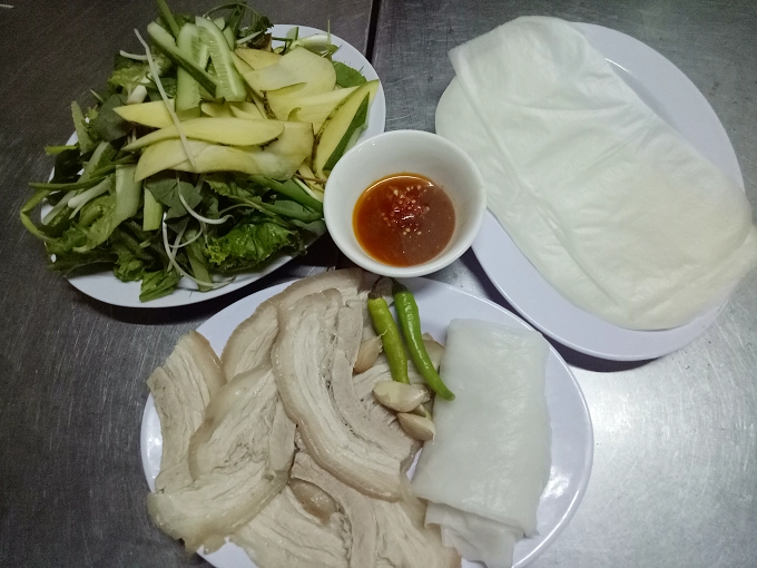 Bánh tráng cuốn thịt heo Khâu chọn lọc nguyên liệu cho món này khá cầu kỳ. Bánh tráng phải là loại phơi sương, thơm mùi gạo. Thịt heo chọn loại ngon, luộc vừa tới rồi ngâm trong nồi nước dùng, sao cho miếng thịt có độ dẻo, phần mỡ trong, phần thịt trắng nõn nà, bì mềm. Trong chợ có tiệm bánh tráng thịt heo của cô Hà (số lô 12 Đình 15A). Suất ăn dành cho một người là 30.000 đồng và 2 người là 50.000 đồng. Bánh tráng cuốn thịt heo Khâu chọn lọc nguyên liệu cho món này khá cầu kỳ. Bánh tráng phải là loại phơi sương, thơm mùi gạo. Thịt heo chọn loại ngon, luộc vừa tới rồi ngâm trong nồi nước dùng, sao cho miếng thịt có độ dẻo, phần mỡ trong, phần thịt trắng nõn nà, bì mềm. Trong chợ có tiệm bánh tráng thịt heo của cô Hà (số lô 12 Đình 15A). Suất ăn dành cho một người là 30.000 đồng và 2 người là 50.000 đồng.