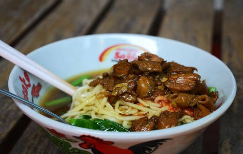 Mie ayam (Mì gà) Mì là món ăn có xuất xứ từ Trung Quốc và phổ biến ở hầu hết quốc gia Đông Nam Á. Ở Indonesia, mie ayam hay mì gà được coi là món ăn nổi tiếng của người Indonesia gốc Hoa. Với các nguyên liệu đơn giản từ mì, gà, rau cải, hành lá và các gia vị đi kèm, món ăn có thể làm bữa chính cũng như bữa phụ. Sợi mì màu vàng sau khi trụng chín được trộn với nước tương, tỏi và dầu ăn. Dầu có thể là chất béo hoặc dầu thực vật có tác dụng để tách các sợi mì. Thịt gà được cắt miếng nhỏ và nấu cùng với nước tương, tỏi và các nguyên liệu khác. Món ăn khi đem ra rất bắt mắt với thịt gà, hỗn hợp nấm, hành lá bên trên, và thường kèm với một bát súp nhỏ được nấu từ xương gà. Thoạt nhìn có vẻ đơn giản nhưng hương vị đậm đà được ướp trong thịt gà cùng với bát súp nhỏ thanh ngọt sẽ khiến bạn không khỏi xuýt xoa. Giá cho một tô mì gà từ 6.000 rupiah (khoảng 10.000 đồng). Ảnh: Phong Vinh.