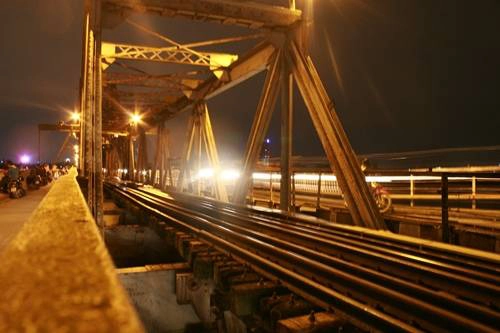 Những buổi tối, cây cầu hơn 100 tuổi Long Biên lại nhộn nhịp những bạn trẻ thong dong tản bộ, tạm xa dần ánh sáng thành thị và ngắm nhìn màn đêm buông. Âm thanh của cuộc sống vang lên với tiếng còi tàu hỏa, tiếng những vòng quay xe đạp của những người buôn bán từ khắp nơi trở về nhà sau ngày làm lụng vất vả. Bạn có thể sà vào một hàng ngô khoai nướng mới dọn hàng để tạm quên đi cái giá rét của mùa đông Hà Nội. Ảnh: Minh Đức Những buổi tối, cây cầu hơn 100 tuổi Long Biên lại nhộn nhịp những bạn trẻ thong dong tản bộ, tạm xa dần ánh sáng thành thị và ngắm nhìn màn đêm buông. Âm thanh của cuộc sống vang lên với tiếng còi tàu hỏa, tiếng những vòng quay xe đạp của những người buôn bán từ khắp nơi trở về nhà sau ngày làm lụng vất vả. Bạn có thể sà vào một hàng ngô khoai nướng mới dọn hàng để tạm quên đi cái giá rét của mùa đông Hà Nội. Ảnh: Minh Đức