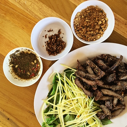 Bò khô muối kiến Bò khô chấm cùng muối kiến là món ăn kích thích sự tò mò của nhiều khách phương xa. Thịt được thái thành từng miếng to cỡ bằng bàn tay rồi tẩm ướp gia vị đem nướng. Chủ quán khéo léo để thịt không quá cháy, vẫn giữ được độ ngọt, dai và không bị khô. Món ăn này sẽ tròn vị nếu bạn chấm cùng với muối được chế biến từ loại kiến vàng sống trên cây rừng hay ở các vườn. Độ thơm, ngọt của thịt bò quyện cùng vị chua đặc trưng của muối kiến khiến bạn muốn ăn mãi không thôi. Bạn có thể mua món ăn này về làm quà tặng bạn bè, người thân, giá một kg thịt bò khoảng 500.000 đồng. Bò khô muối kiến Bò khô chấm cùng muối kiến là món ăn kích thích sự tò mò của nhiều khách phương xa. Thịt được thái thành từng miếng to cỡ bằng bàn tay rồi tẩm ướp gia vị đem nướng. Chủ quán khéo léo để thịt không quá cháy, vẫn giữ được độ ngọt, dai và không bị khô. Món ăn này sẽ tròn vị nếu bạn chấm cùng với muối được chế biến từ loại kiến vàng sống trên cây rừng hay ở các vườn. Độ thơm, ngọt của thịt bò quyện cùng vị chua đặc trưng của muối kiến khiến bạn muốn ăn mãi không thôi. Bạn có thể mua món ăn này về làm quà tặng bạn bè, người thân, giá một kg thịt bò khoảng 500.000 đồng.