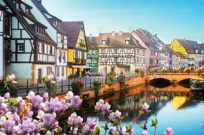 Thị trấn Colmar, Pháp  Những căn nhà gỗ half-timeber vài trăm tuổi có mái dốc, lợp ngói nâu đỏ cùng mảng tường đủ màu chính là điểm nhấn nổi bật thu hút hàng triệu du khách mỗi năm đến thị trấn Colmar. Khắp nơi, từ khung cửa cho đến bờ tường hay chiếc cầu bắc qua sông, bạn đều thấy sự hiện diện của cây cỏ, hoa lá.  Mỗi góc phố ở Colmar đều là góc ảnh đầy chất thơ. Mỗi ngôi nhà là một tác phẩm nghệ thuật để bạn thỏa sức ghi lại những khoảnh khắc kỷ niệm. Ảnh: Shutterstock/Neirfy.