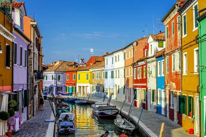 Đảo Burano, Italy  Hòn đảo nhỏ ngoài khơi thành phố Venice được ví như viên ngọc giữa biển khơi. Mỗi ngôi nhà có một sắc màu riêng độc đáo. Do ngư dân không thể nhận ra nhà mình giữa lúc rạng đông sương mờ nên đã sơn nhà bằng nhiều màu. Ngày nay, nếu muốn sơn lại nhà, họ phải xin phép chính quyền và chỉ sơn một số màu chỉ định.  Du khách đến đây có thể leo lên thuyền để đi dọc dòng kênh xanh biếc, ngắm nhìn hình ảnh phản chiều của dãy nhà sặc sở ở hai bên bờ. Đảo khá nhỏ lại yên tĩnh, ít hàng quán nên rất hợp cho những tâm hồn thơ mộng. Ảnh: Shutterstock/Alexandra Lande.