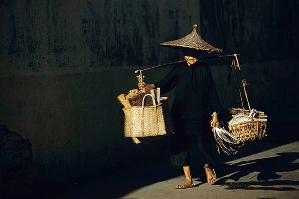 Một cụ bà với chiếc gánh bàn chải, chổi và quạt trên vai.