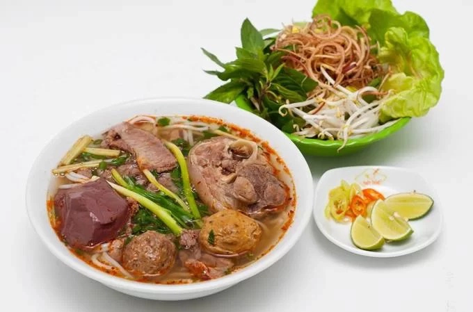 Bún bò Chú Há  Quán nằm ở đường Võ Văn Tần (quận 3), gần đoạn giao với đường Nguyễn Thượng Hiền. Nằm giữa dãy nhà mặt phố, quán có đặc điểm nhận dạng là một chiếc xe đẩy nhỏ, bên trên chất đầy các loại nguyên liệu, được che chắn bởi một tấm kính. Chủ quán là người vui tính, sẽ tự tay nấu cho bạn tô bún bò. Khi có khách gọi món, chủ sẽ trụng những sợi bún rồi cho vào tô trước khi xếp lên trên các loại nguyên liệu như chả, thịt bò, giò... Không cần trang trí thêm, tô bún bò đã đủ hấp dẫn nhờ vị nước lèo. Chủ quán kết hợp cách thức nấu nướng của người Hoa vào món ăn truyền thống của người Huế. Giá một suất ăn ở đây khoảng 60.000 đồng. Ảnh: Di Vỹ.