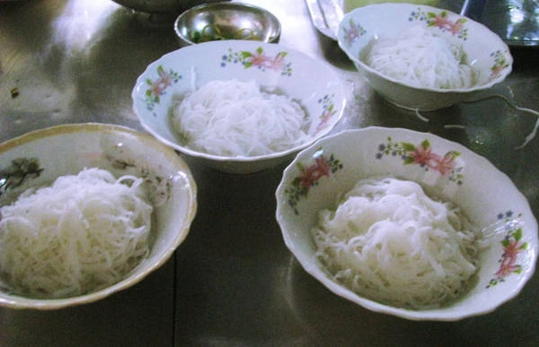 Bún ép ra trên nồi nước gạo đun sôi rồi vớt ra để ráo, cho vào tô. Bún ép ra trên nồi nước gạo đun sôi rồi vớt ra để ráo, cho vào tô.