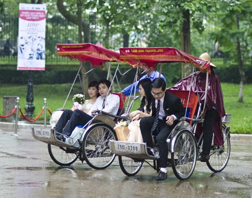 Trong cơn mưa nhỏ, các đôi uyên ương được diễu hành qua các con phố Hà Nội bằng xích lô trước khi đến địa điểm thi.