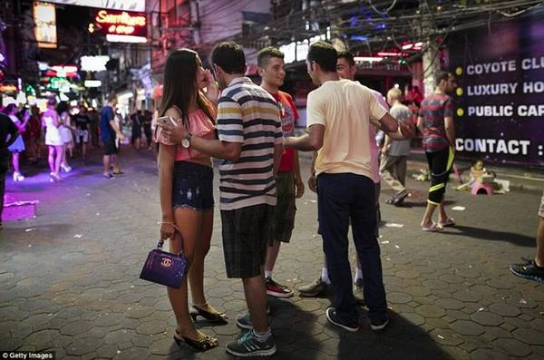 Một cô gái làm ở quán bar trong trang phục mát mẻ trò chuyện với nam du khách trên phố.