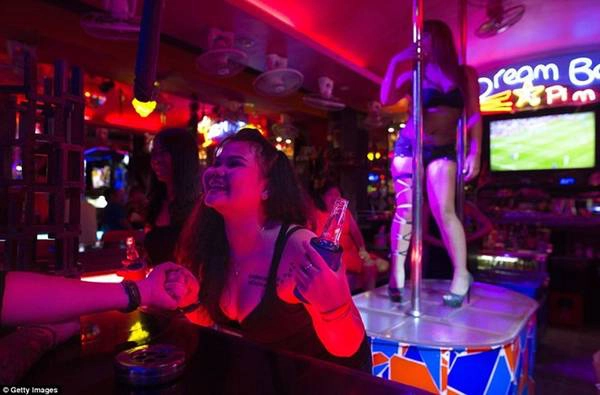Những người phụ nữ làm việc trong quán bar trò chuyện với khách hàng và múa cột trong lúc các trận bóng đá được chiếu trên màn hình lớn.