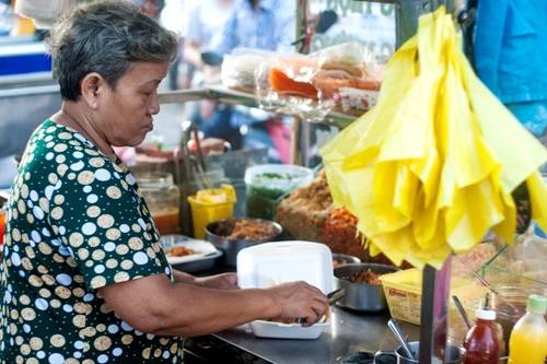 Cạnh đó là một bác bán hàng lớn tuổi đang làm món bánh tráng trộn cho nhóm khách du lịch nước ngoài. Bánh tráng trộn là món ăn đặc sản Sài Gòn và các tỉnh miền Nam mà bạn không nên bỏ qua.