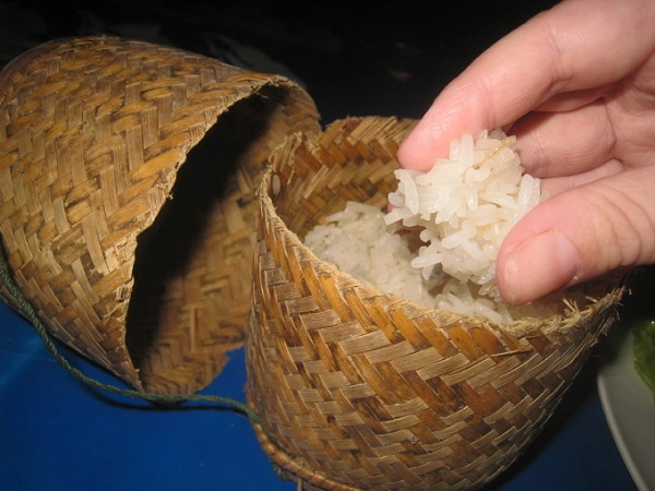Khao Niaw (Xôi) nấu từ gạo dẻo, màu trắng ngà là món không thể thiếu trong tất cả các bữa ăn ở đây. Xôi được đựng trong một giỏ nhỏ đan bằng tre đơn giản, mộc mạc. Ăn đúng kiểu Lào là phải dùng tay nén thành viên tròn rồi mới cho vào miệng - Ảnh: mmmgoodfood Khao Niaw (Xôi) nấu từ gạo dẻo, màu trắng ngà là món không thể thiếu trong tất cả các bữa ăn ở đây. Xôi được đựng trong một giỏ nhỏ đan bằng tre đơn giản, mộc mạc. Ăn đúng kiểu Lào là phải dùng tay nén thành viên tròn rồi mới cho vào miệng - Ảnh: mmmgoodfood