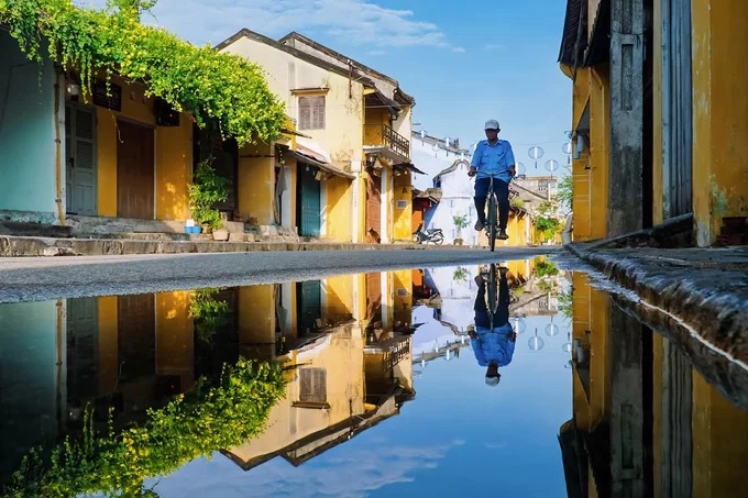 “Sau mưa, khi nước còn đọng lại trên nền đường là lúc tôi háo hức lang thang khắp Hội An ghi lại vẻ đẹp trầm lặng, cuốn hút của cảnh vật và con người phố cổ. Cái khó nhất của kiểu chụp này là bóng phải rõ nét trên nền nước, màu sắc tương phản giữa ảnh thật và bóng cân bằng, không lệch nhau quá”, anh Vũ nói.