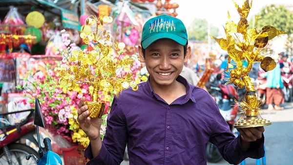 Một thanh niên cười tươi bên cạnh những món đồ trong gian hàng của mình.