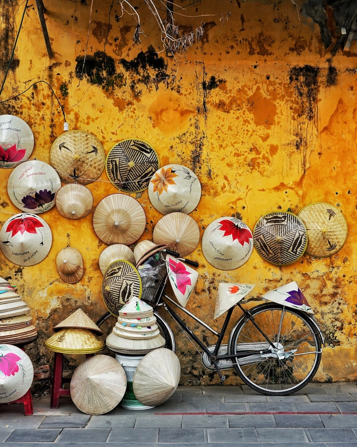 Một shop bán nón lá trưng bày bên cạnh mảng tường màu vàng đặc trưng ở Hội An - Ảnh: Chris Schalkx