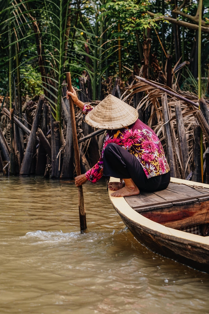 Người phụ nữ lớn tuổi đội nón lá chèo xuồng trên một kênh rạch ở đồng bằng sông Cửu Long - Ảnh: Chris Schalkx