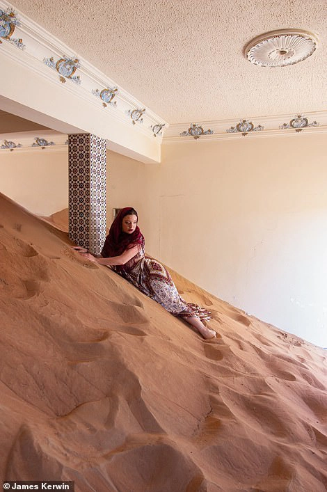 Một số ngôi nhà bị cát lấp cao tới gần chạm nóc. Trong ảnh, nhiếp ảnh gia Jade đang nằm trên cát chụp hình.