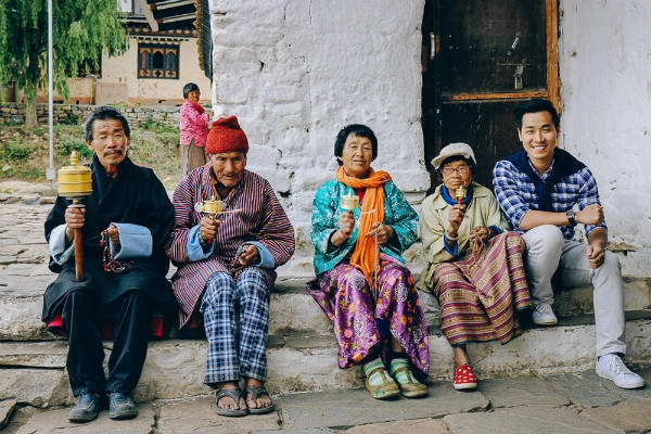 Nguyên Khang chụp ảnh cùng với những người dân Bhutan. Trên tay họ đang cầm Kim Luân Chuyển Chú – một tín vật của Phật Giáo Bhutan. Người già ở Bhutan thường dành thời gian đi đến chùa đọc kinh và thực hiện đều đặn mỗi ngày.
