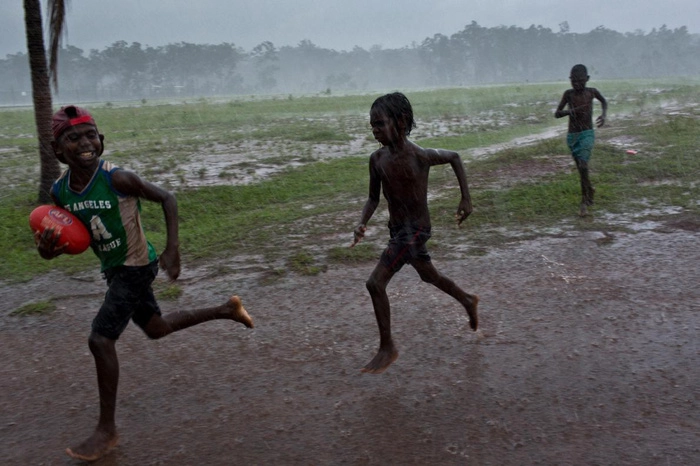 Một nhóm trẻ em chơi môn bóng đá kiểu Úc trong mưa tại khu dân cư Pirlangimpi, đảo Melville - Ảnh: DAVID MAURICE SMITH, OCULI/NG