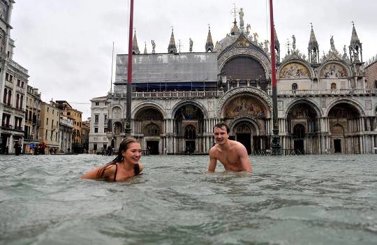 Một người đàn ông và một phụ nữ bơi trong dòng nước lụt ở Piazza San Marco (quảng trường Thánh Mark) tại Venice, Italy, 11/11/2012. Triều cường đã làm ngập lụt Venice, buộc người dân Venice và du khách phải mang ủng cao hoặc dùng các lối đi bằng gỗ để đi lại ở quảng trường Piazza San Marco cũng như các nơi bị ngập khác.