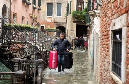 Một người mang hành lý đi qua dòng nước lụt ở Venice, 01/11/2012.