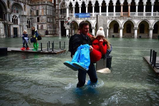 Một người đàn ông ẵm cô gái khi họ đi khỏi dòng nước lũ ở Piazza San Marco, Venice, 01/11/2012.