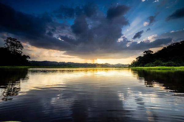 Hoàng hôn trên Bàu Sấu. Ánh mặt trời hừng lên từ đám mây đen ở rặng núi phía xa. Hoàng hôn trên Bàu Sấu. Ánh mặt trời hừng lên từ đám mây đen ở rặng núi phía xa.