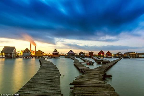 Nhà máy điện rực sáng phía bên kia hồ nước tương phản với khung cảnh trên mặt nước im lìm, tĩnh lặng của ngôi làng.