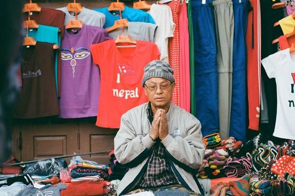 Một người buôn bán quần áo ở Kathmandu hướng về bảo tháp để cầu nguyện. Với người dân ở đây, việc thực hành hàng ngày tự nhiên như hơi thở. Một người buôn bán quần áo ở Kathmandu hướng về bảo tháp để cầu nguyện. Với người dân ở đây, việc thực hành hàng ngày tự nhiên như hơi thở.